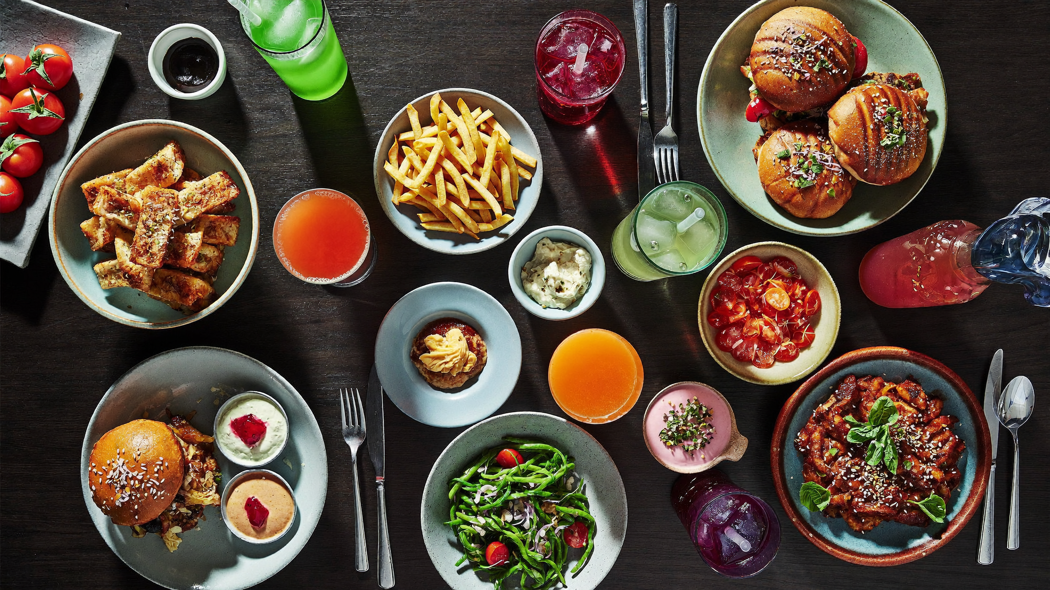 Overhead view of a full table with burgers, pizza, pasta, fries, desserts and drinks